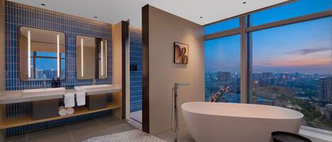 A modern bathroom with a large bathtub, a vanity with a mirror, and a city view through large windows.