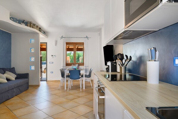 A modern kitchen with a dining area, a sofa, and a view through the window.