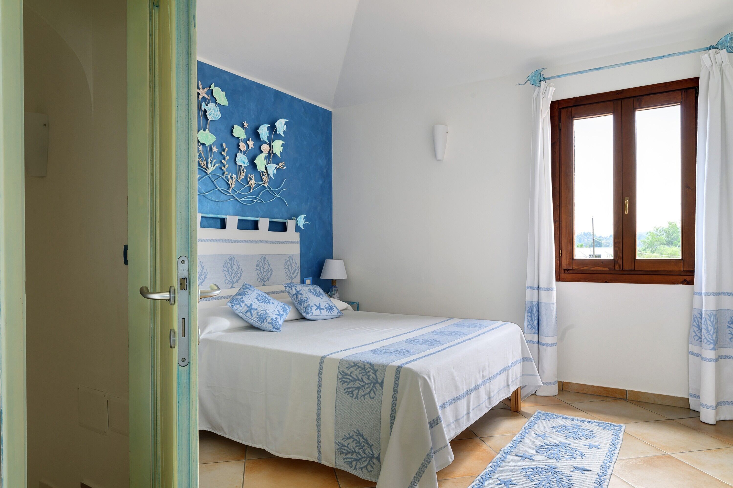 Ein Schlafzimmer mit einem Bett, einem Nachttisch, einer Lampe und einem Fenster mit Vorhängen.
