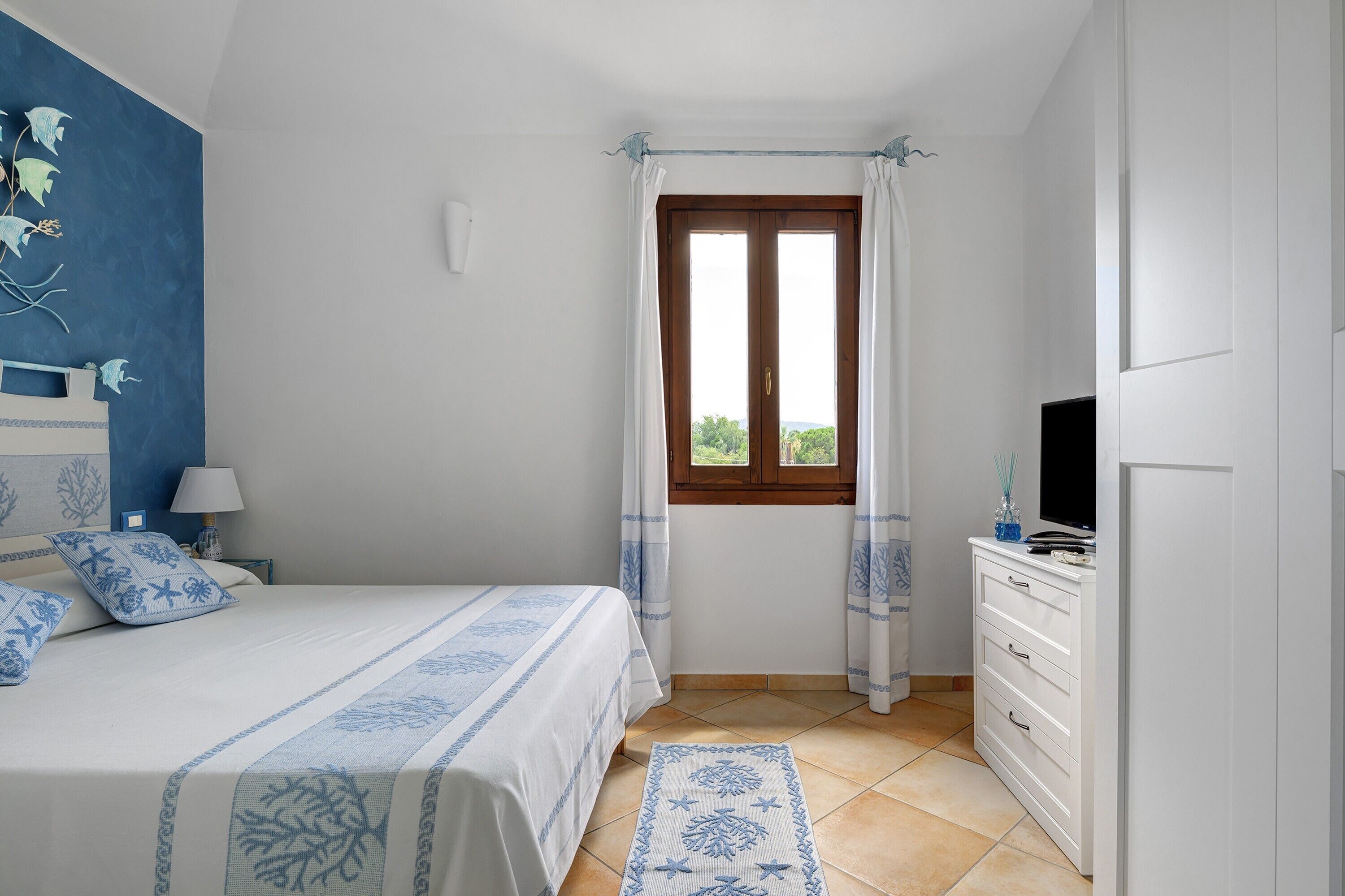 Un dormitorio con cama, cómoda, televisor y ventana con cortinas.
