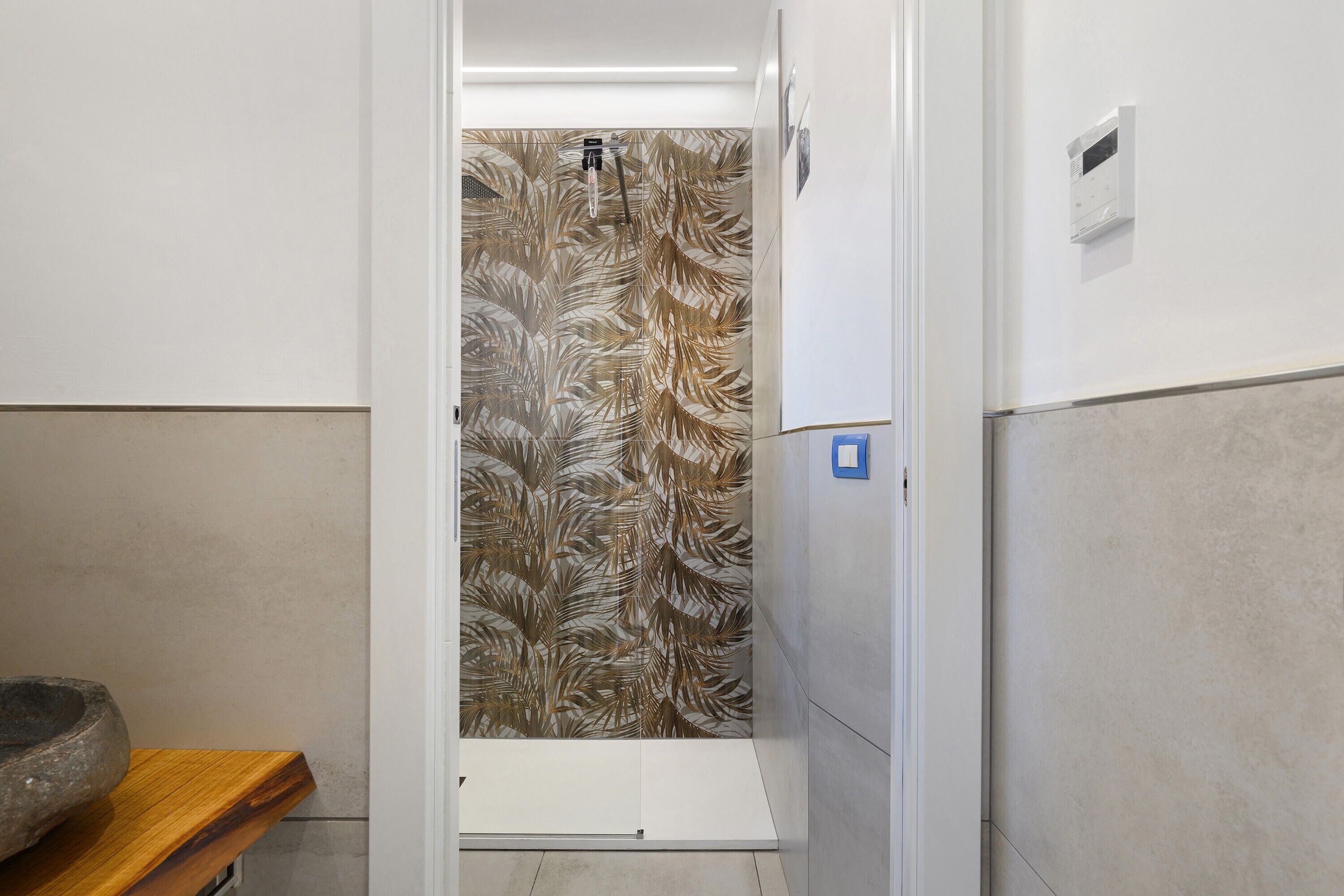 Un bagno con doccia, una panca in legno e una parete decorata con un motivo a foglia.