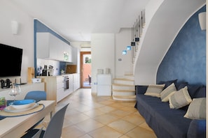 A modern kitchen with white cabinets, a dining area with a table and chairs, a sofa with cushions, and a staircase with a unique design. - Villa Aurora Tortolì Holiday Home with Balcony, Wi-Fi, and Air Conditioning (Tortolì)
