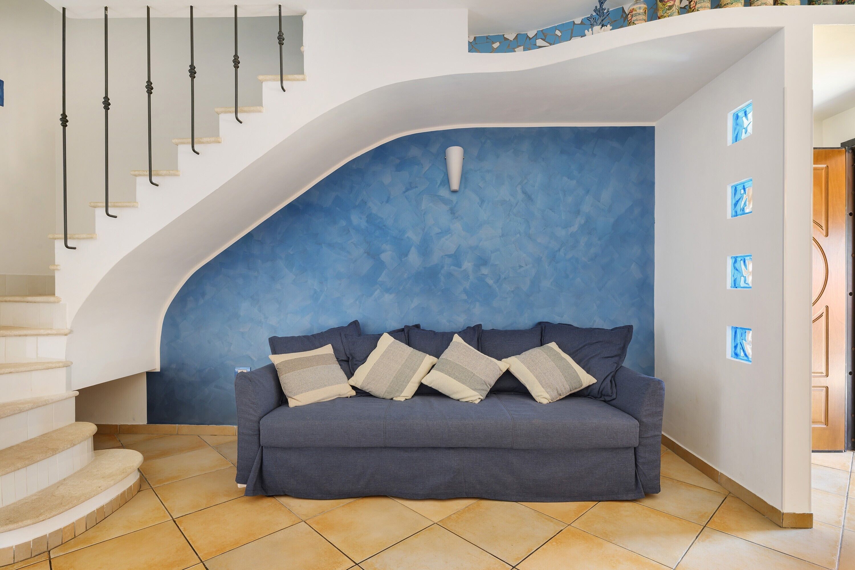 Ein modernes Wohnzimmer mit einer gewölbten Wand, einem grauen Sofa und einer Treppe mit einer weißen Geländer.