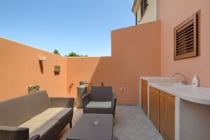 A small outdoor patio with a sofa, a chair, a gas cylinder, and a sink.