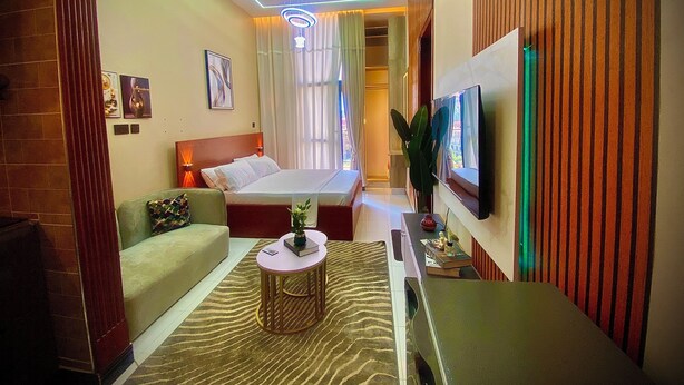 Quarto de hotel com cama, sofá, televisão, mesa pequena e planta.