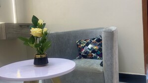 Quarto com sofá cinzento, mesa redonda branca e um vaso de flores amarelas, além de três luminárias fixadas na parede.