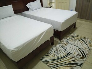 Ein Hotelzimmer mit zwei Einzelbetten, einem gemusterten Teppich und einem Holz-Kopfteil.