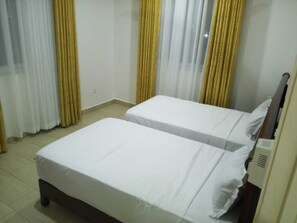 A room with two beds, a window with curtains, and a radiator. - Sun-Drenched Coastal Retreat in Vibrant Mombasa (Mombasa)