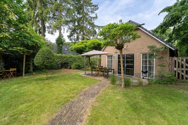 A brick house with a paved pathway leading to a covered patio area with outdoor furniture.