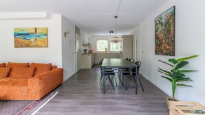 Moderni olohuone, jossa on sohva, ruokapöytä, tuoleja ja taustalla keittiö.