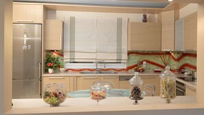 A modern kitchen with a stainless steel refrigerator, wooden cabinets, a glass-top dining table, and a decorative backsplash.