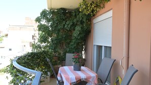 A balcony with a table, chairs, and potted plants.