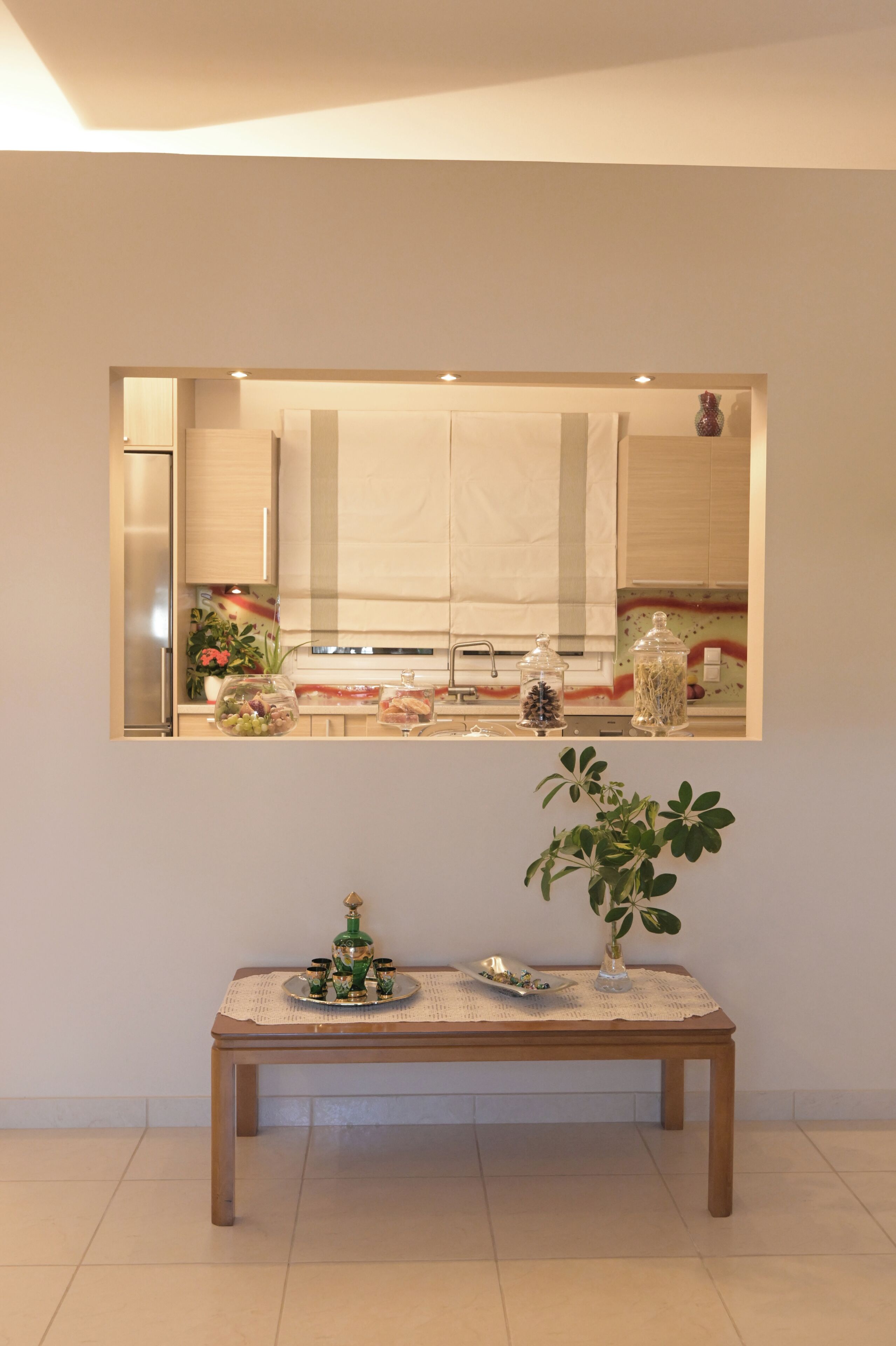 A room with a large mirror, a wooden table with a vase and a tray, and a tiled floor.