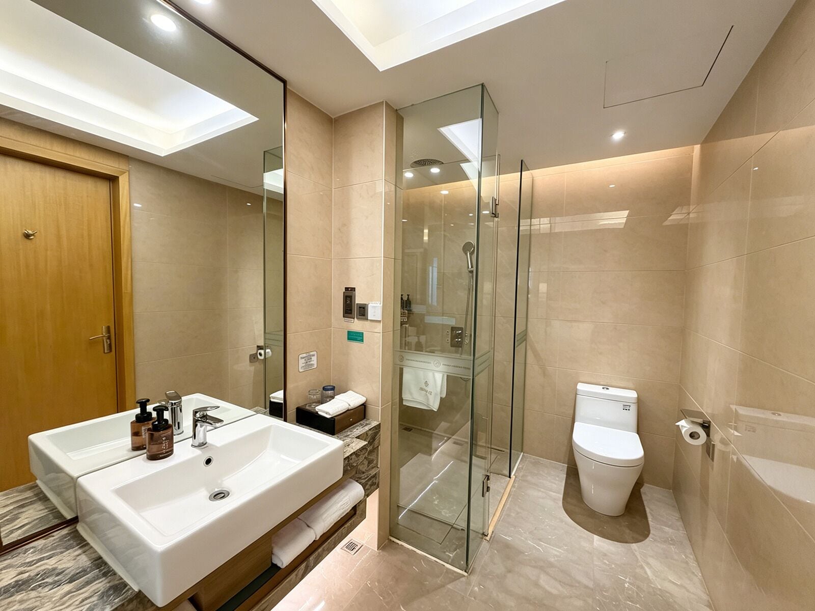 A modern bathroom with a glass shower enclosure, a dual sink vanity, and a toilet.