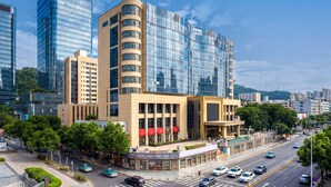 A modern hotel with a glass facade, multiple floors, and a prominent entrance with red awnings. - The Livable Hotel (Shenzhen)