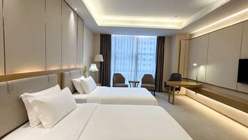 A hotel room with two beds, a desk, a chair, and a TV.