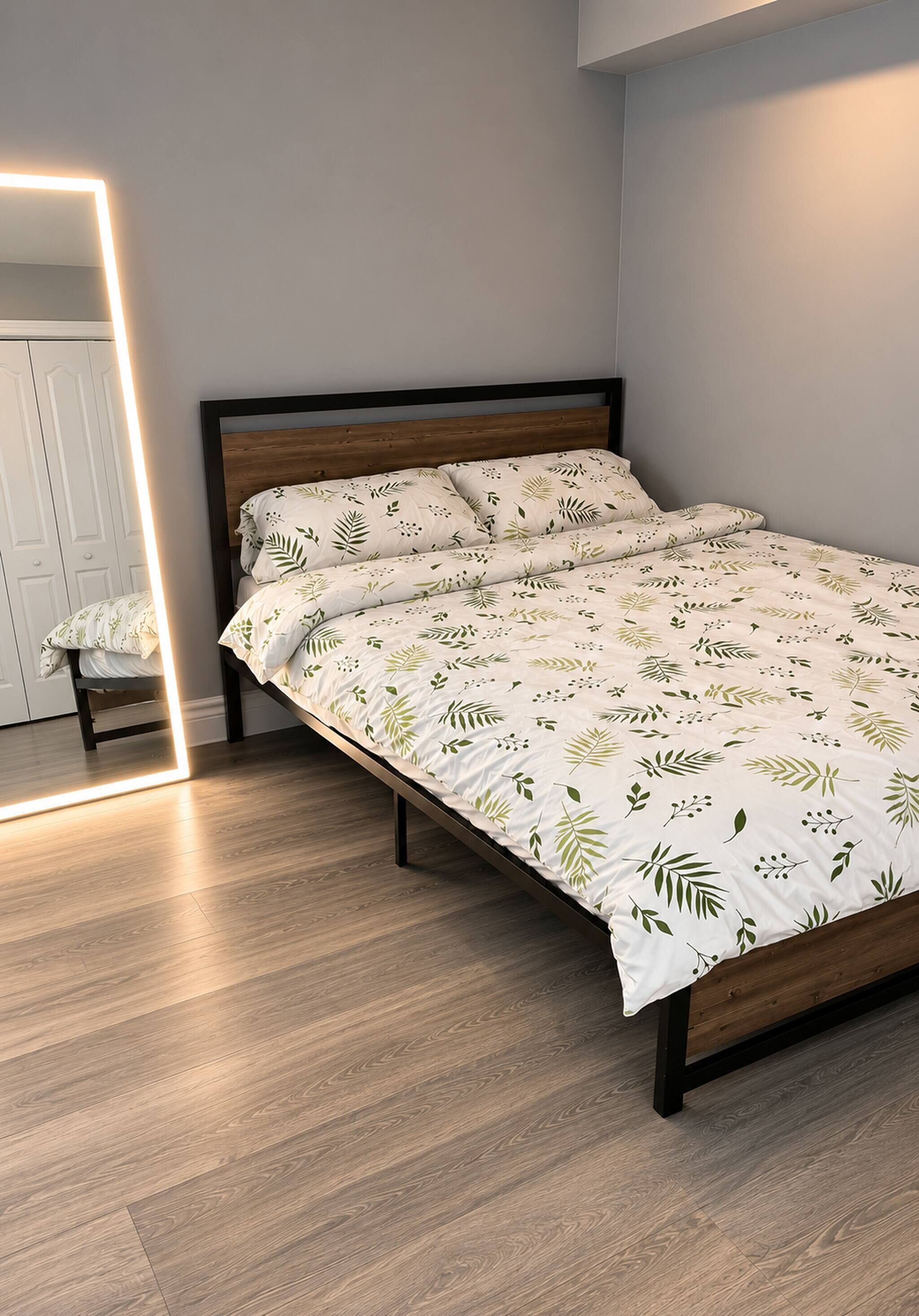 Un lit avec une couvre-lit à motifs de feuilles, une tête de lit en bois et un miroir avec un bandeau lumineux.