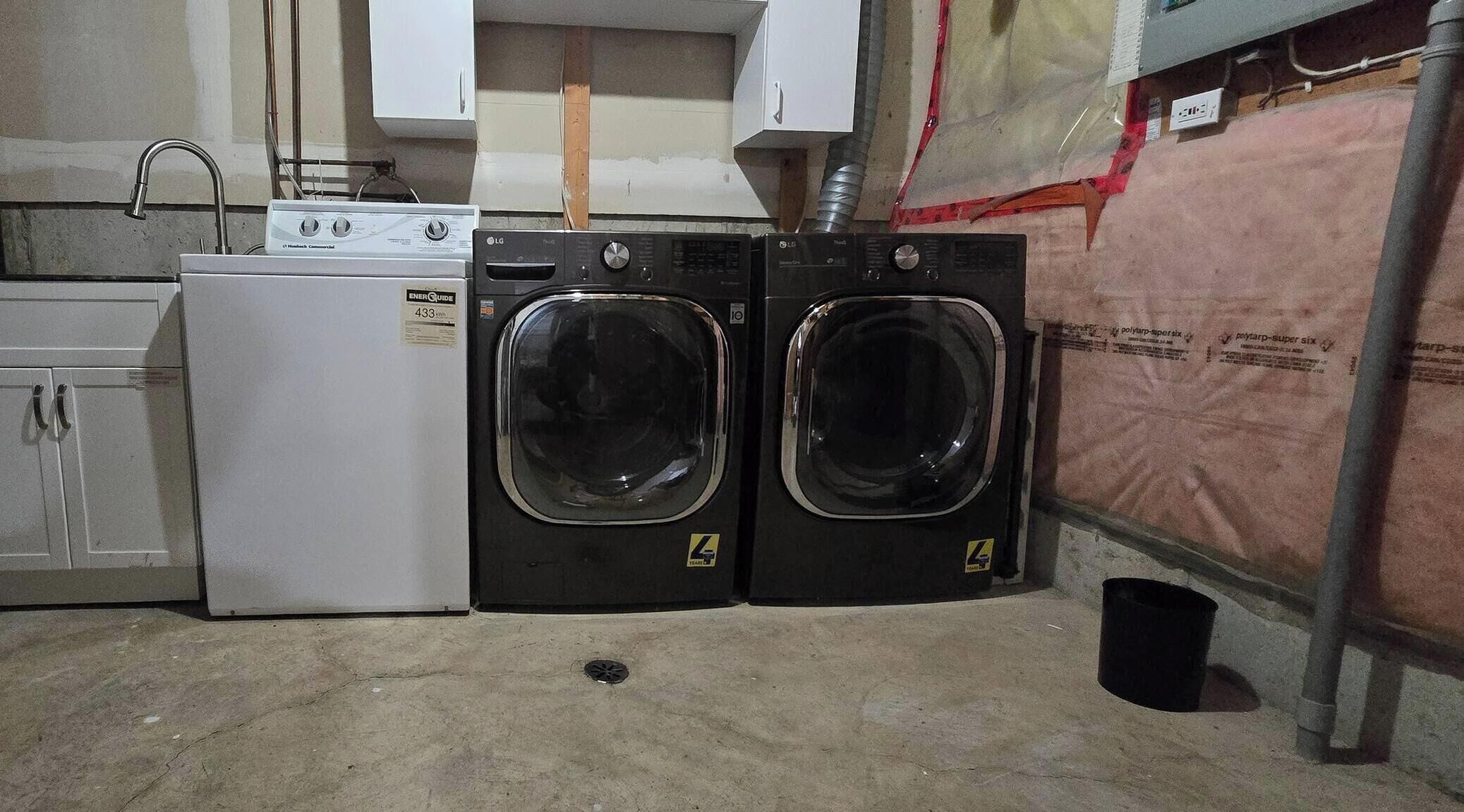 A laundry room with a white washing machine, a dryer, and two stacked black dryers.