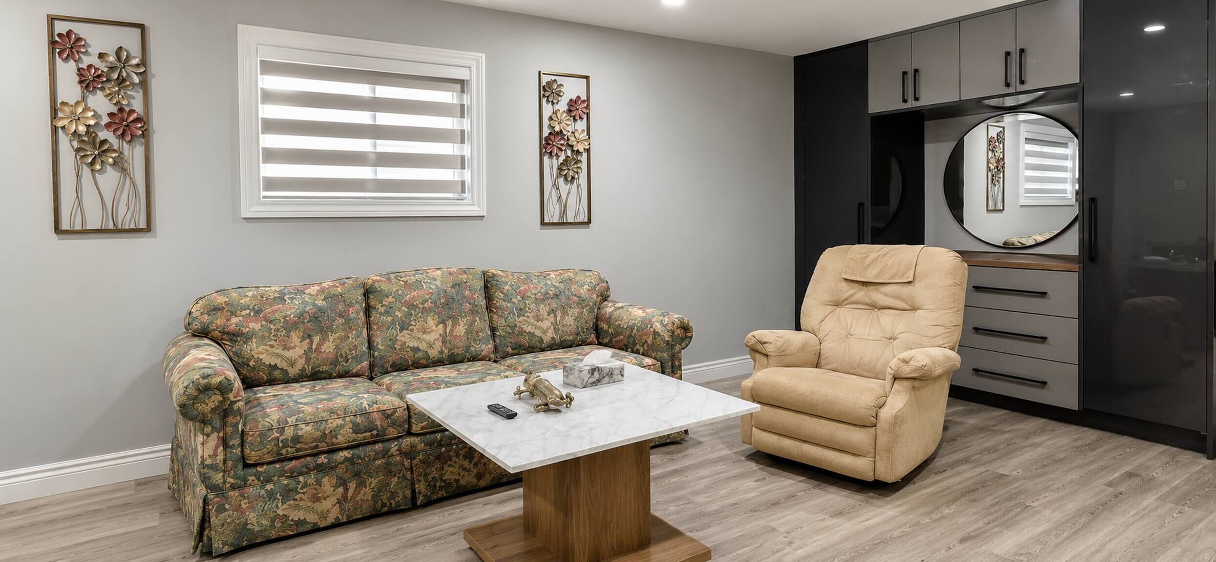 A living room with a floral-patterned sofa, a beige armchair, a marble coffee table, and a black cabinet with a mirror.