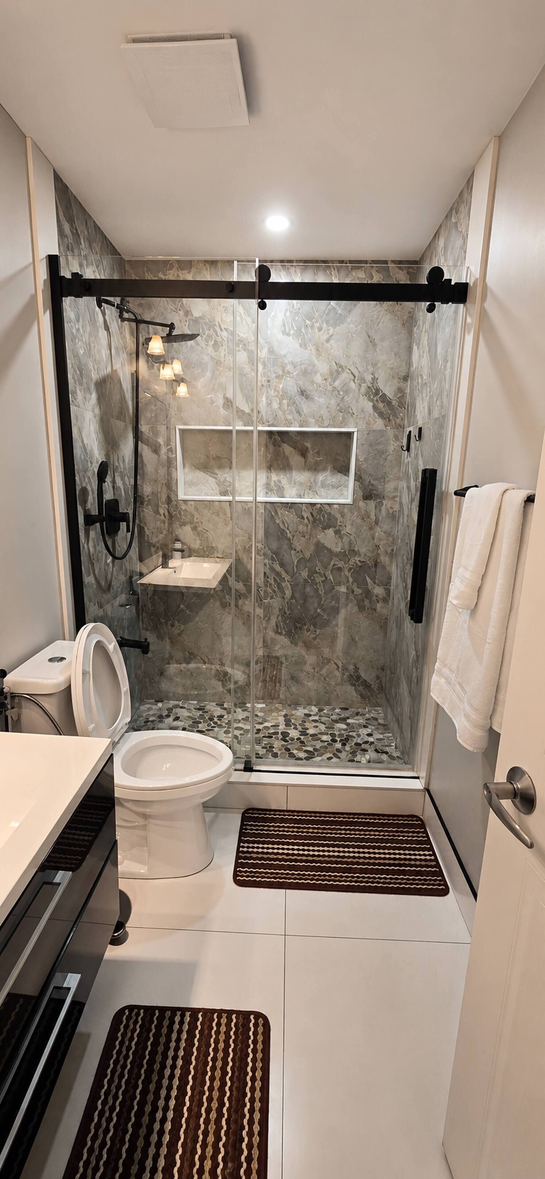 A modern bathroom with a glass-enclosed shower, a toilet, a sink, and a towel rack.