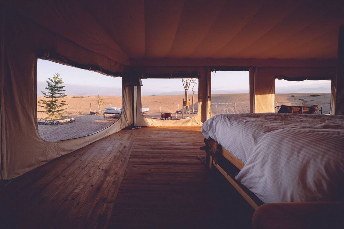 Quarto com tenda, cama e vista para uma paisagem desértica.