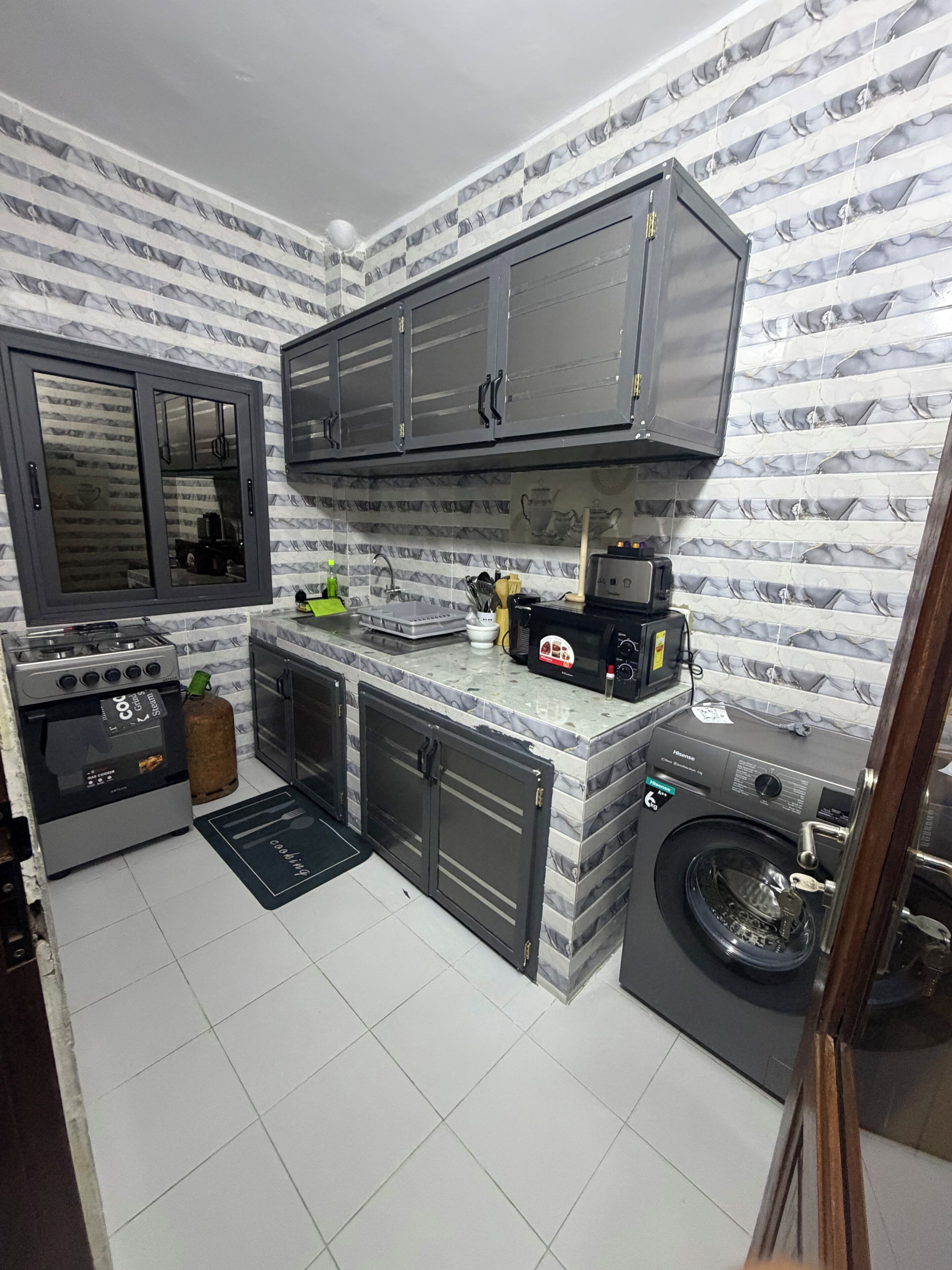 A compact kitchen with a gas stove, a microwave, a washing machine, and a sink.