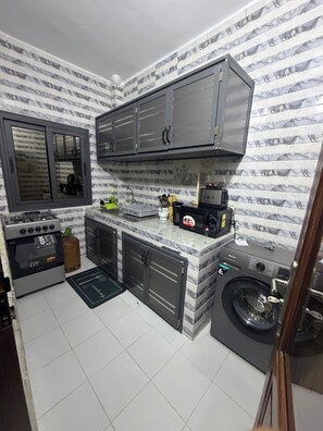 A compact kitchen with a gas stove, a microwave, a washing machine, and a sink. - STUNNING 2-Bedroom Apartment for Rent. (Dakar)
