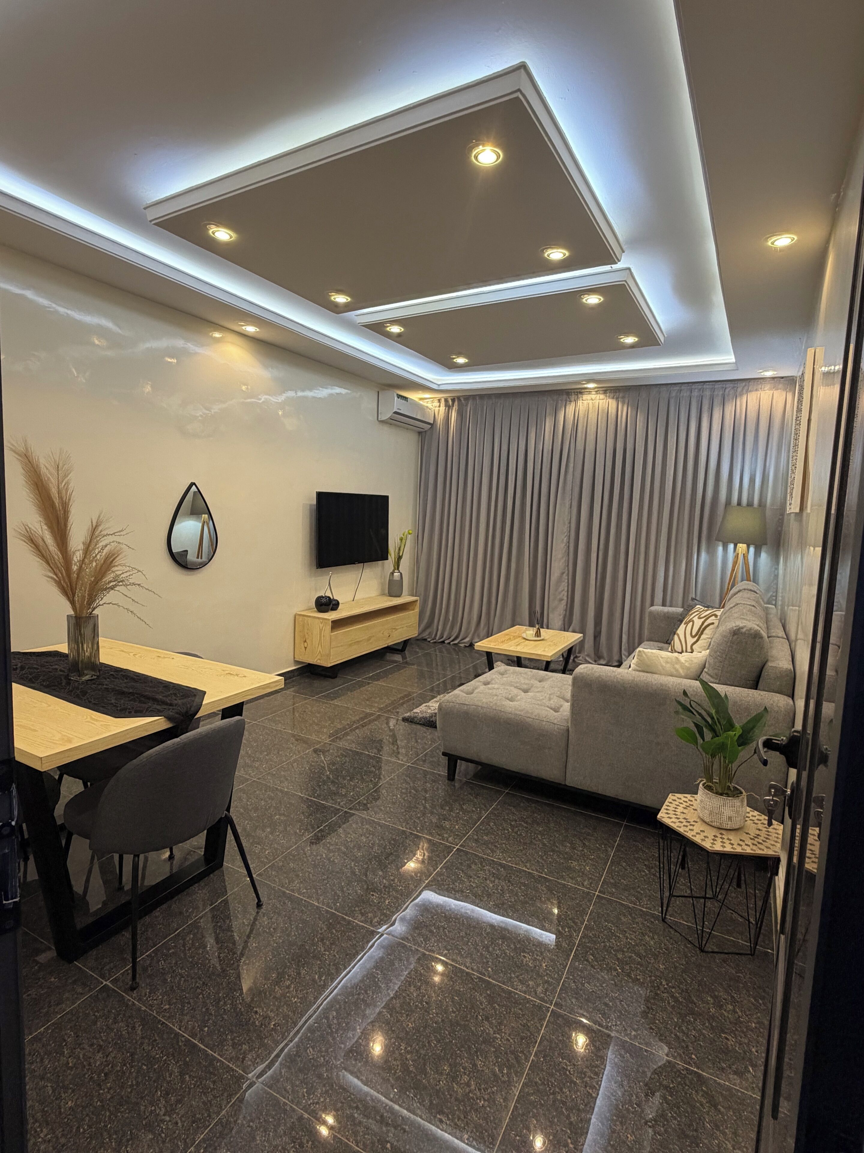 A modern living room with a sofa, a TV, a dining table, and a glass partition.