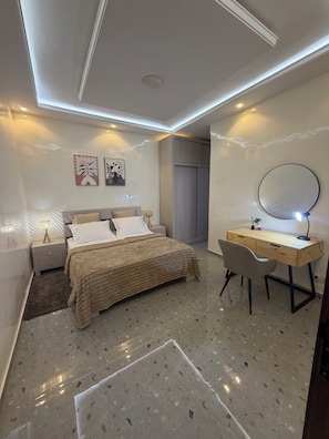 A modern bedroom with a bed, bedside table, desk, chair, and a mirror. - STUNNING 2-Bedroom Apartment for Rent. (Dakar)