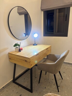 Un bureau en bois, un miroir rond, une lampe de bureau et une chaise.