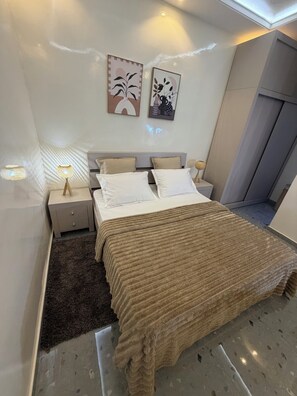 A modern bedroom with a bed, nightstands, a lamp, and artwork on the wall. - STUNNING 2-Bedroom Apartment for Rent. (Dakar)