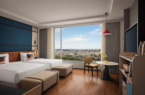 Habitación de hotel con dos camas, un sofá, una mesa de comedor y vistas a la ciudad.