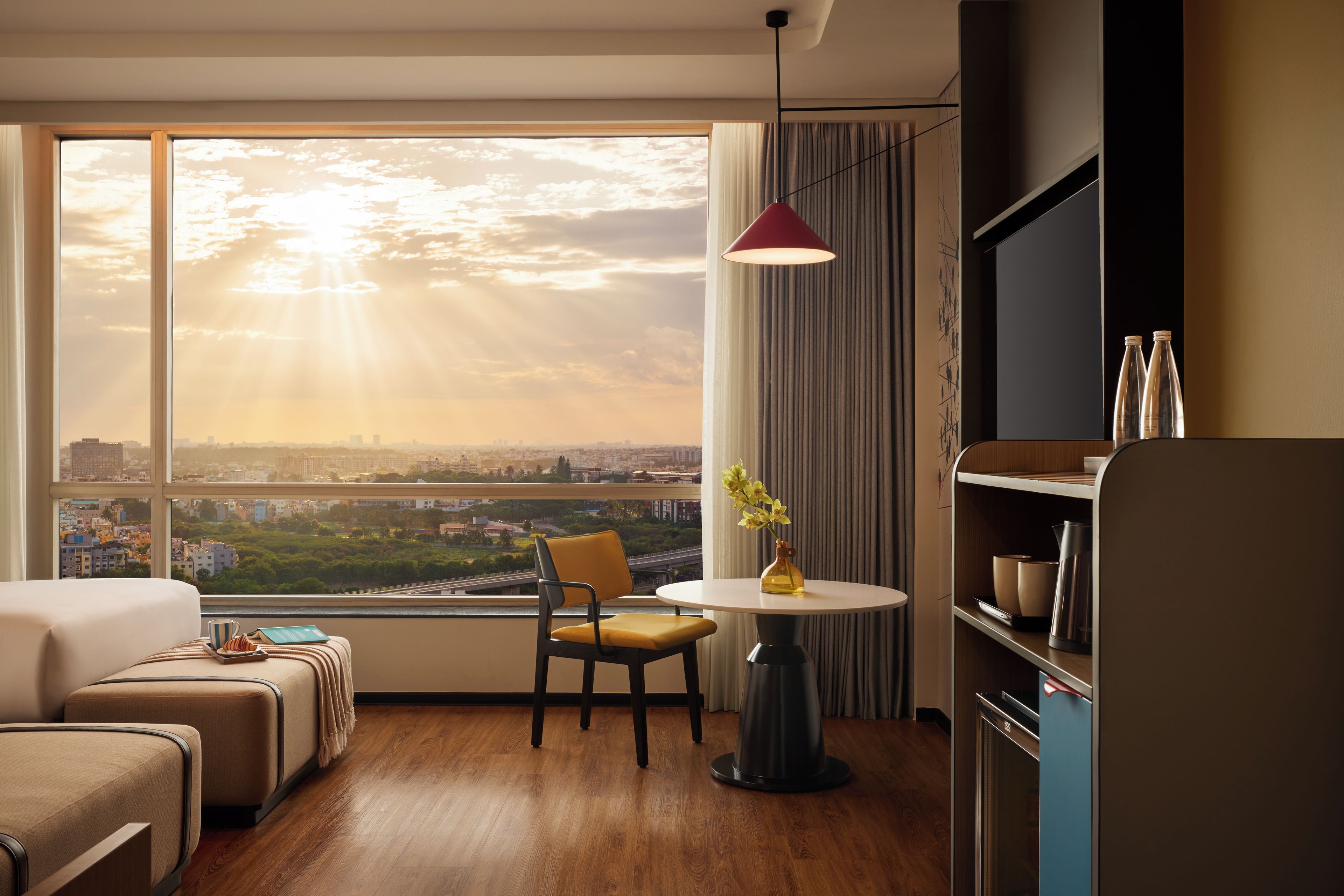 Habitación de hotel con un ventanal grande, una mesa de comedor, una silla, un sofá y un televisor.