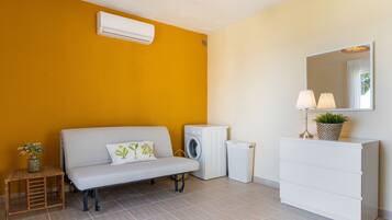 Una habitación con sofá, lavadora, secadora, una mesita con una planta y un aparador con espejo.