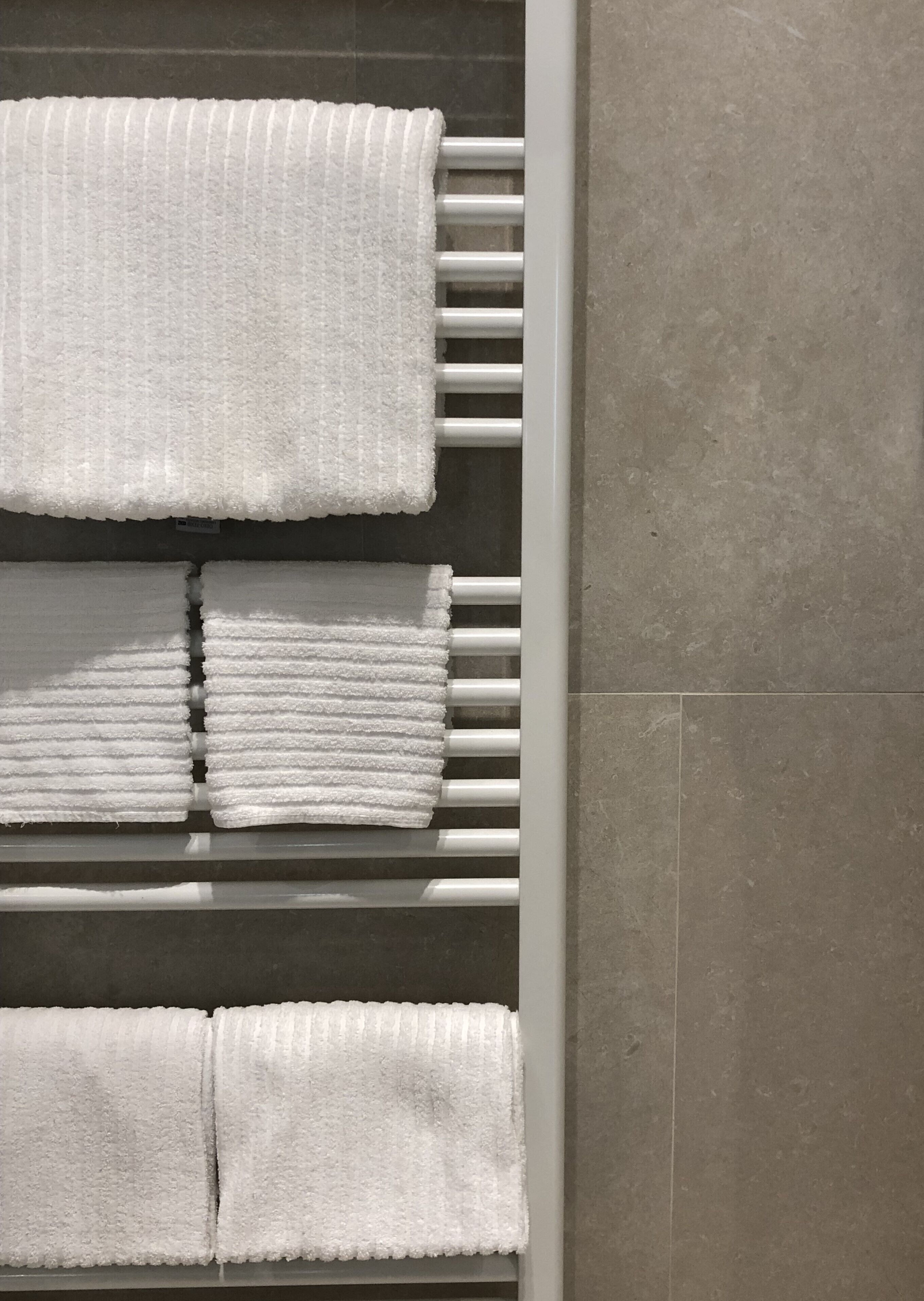 A set of white towels neatly arranged on a white towel rack against a tiled wall.