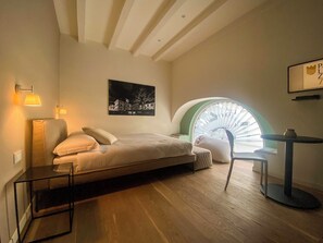 A bedroom with a bed, bedside lamps, a chair, a small table, a picture on the wall, and a skylight. - Palazzo7 (DOMODOSSOLA)