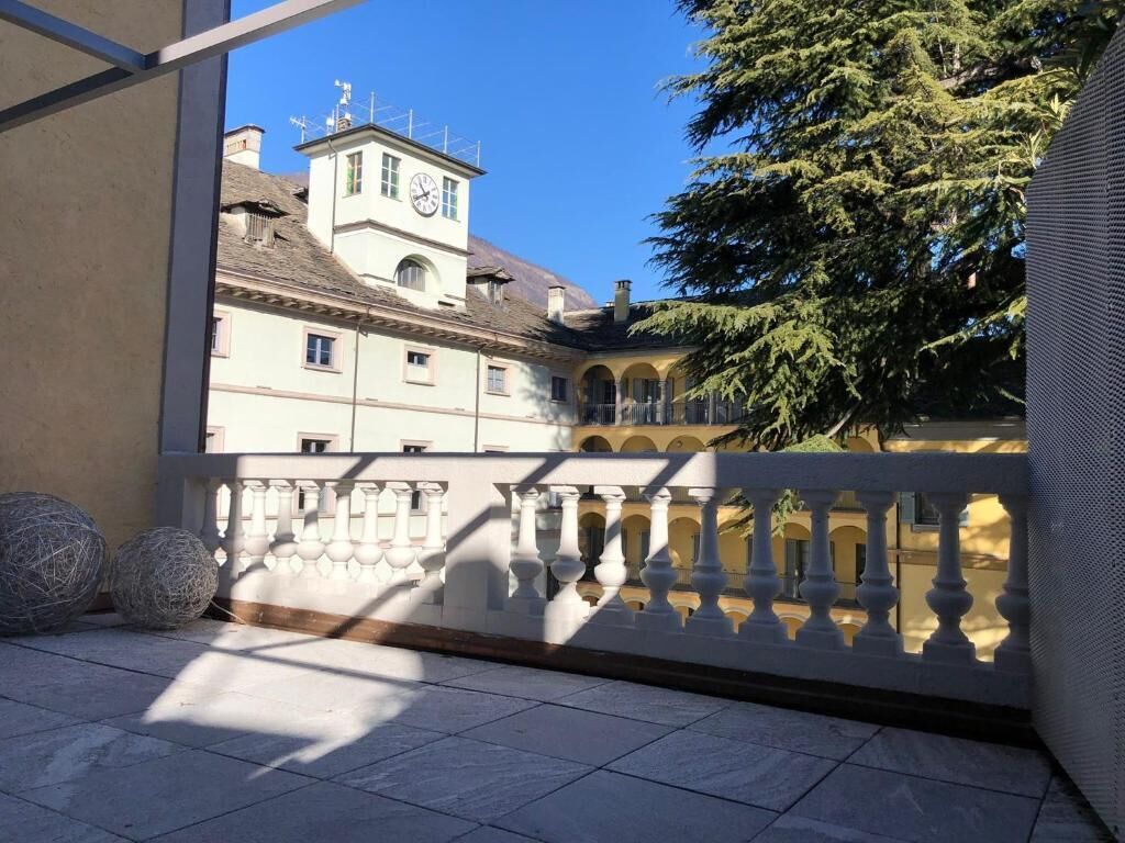 A balcony with a view of a building with a clock tower, a tree, and a white balustrade.