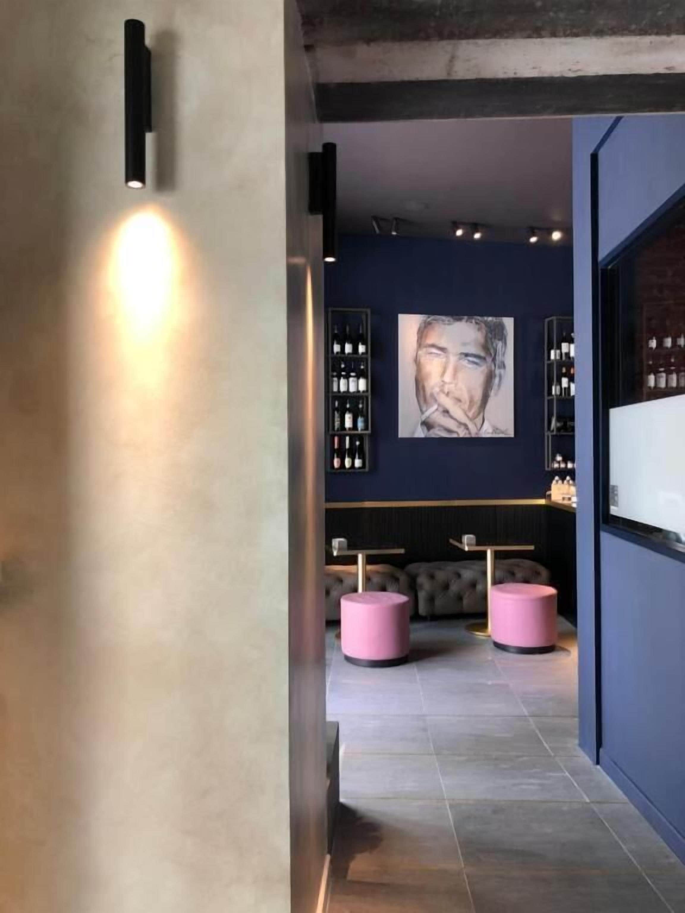 A modern interior with a dark blue wall, a large abstract painting, and a bar area with bottles.