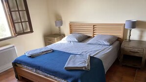 Ein Bett mit blauer Decke, zwei Kissen und einem hölzernen Kopfteil. Es gibt zwei Nachttische mit Lampen.