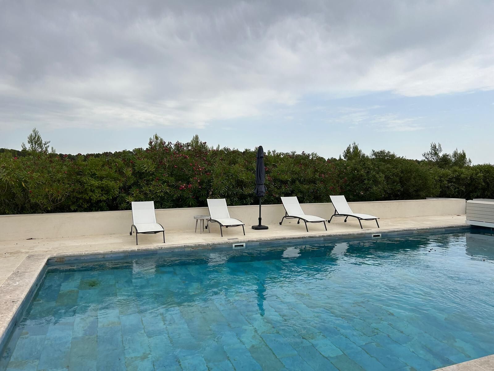 Una piscina con cuatro sillas reclinables y una mesa, rodeada por un seto bajo.