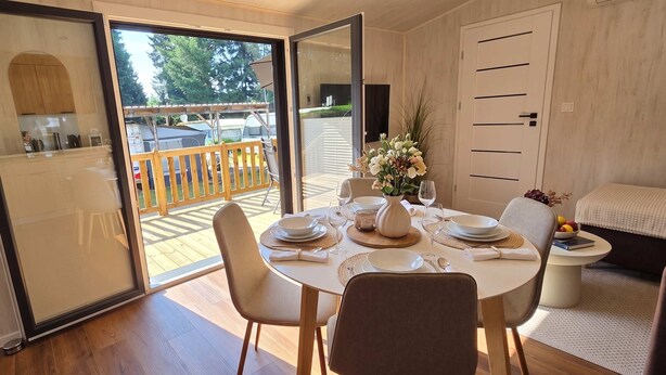 A dining area with a table set for four, a sofa, and a view of the outdoors. - Tinyhouse „SeeZeit“ in ruhiger, naturnaher Lage direkt am Garder See. (Lohmen)