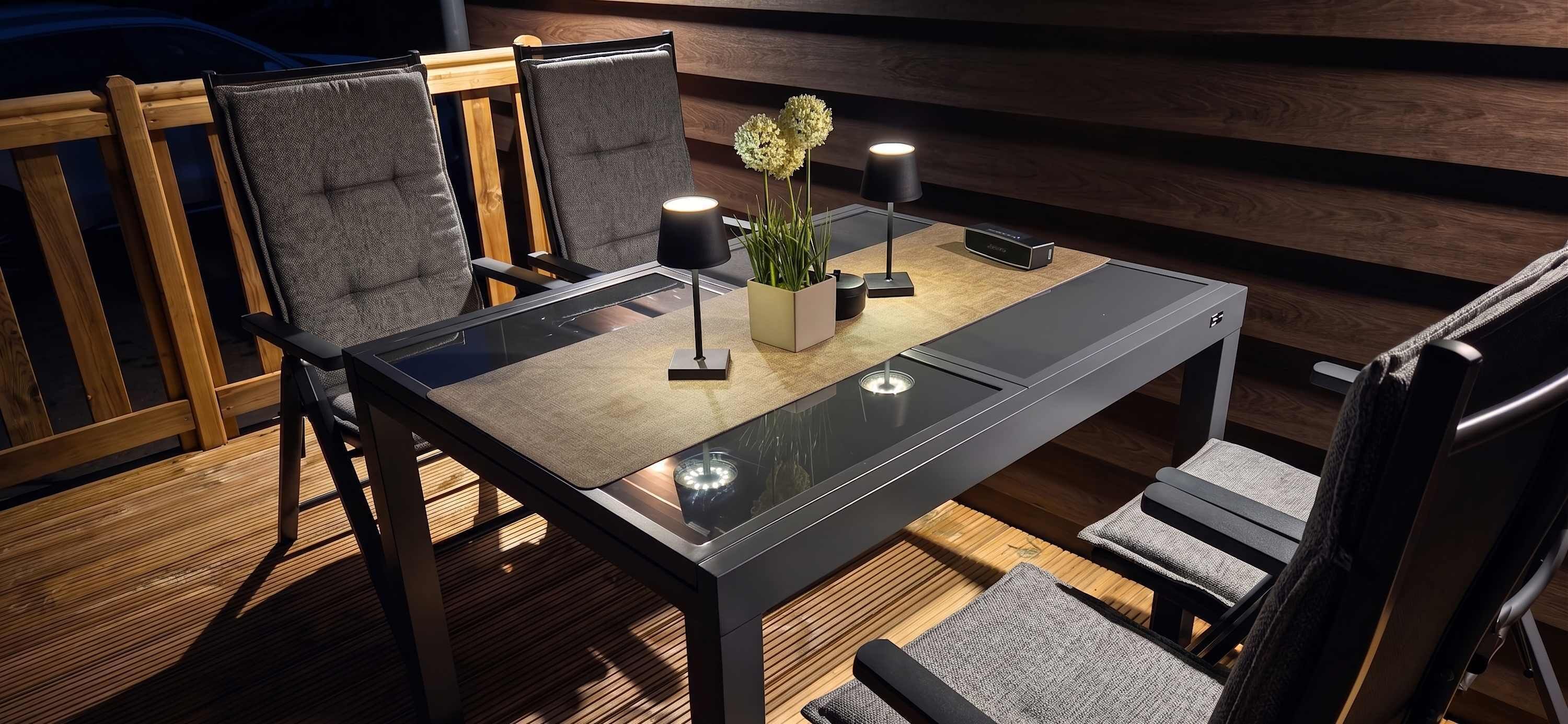 Ein moderner Essbereich mit einem Glastisch, gepolsterten Stühlen, einer kleinen Tischlampe, einem Blumentopf und einer Fernbedienung auf dem Tisch.