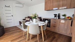A modern kitchen with wooden cabinets, a dining table set for four, and a small potted plant on the counter. - Tinyhouse „SeeZeit“ in ruhiger, naturnaher Lage direkt am Garder See. (Lohmen)