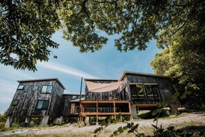 Una cabaña de madera moderna con terraza, rodeada de árboles y un cielo despejado.