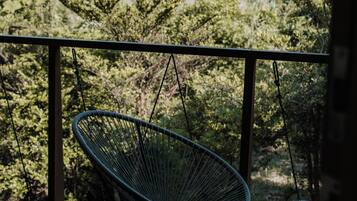 Eine Holzterrasse mit einem Metallschaukelstuhl und einem kleineren Stuhl, mit Blick auf eine gebirgige Landschaft.
