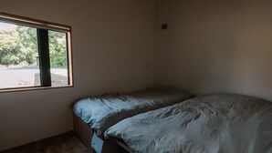 Una habitación pequeña con cama individual, ventana, suelo de madera y una cama sencilla.