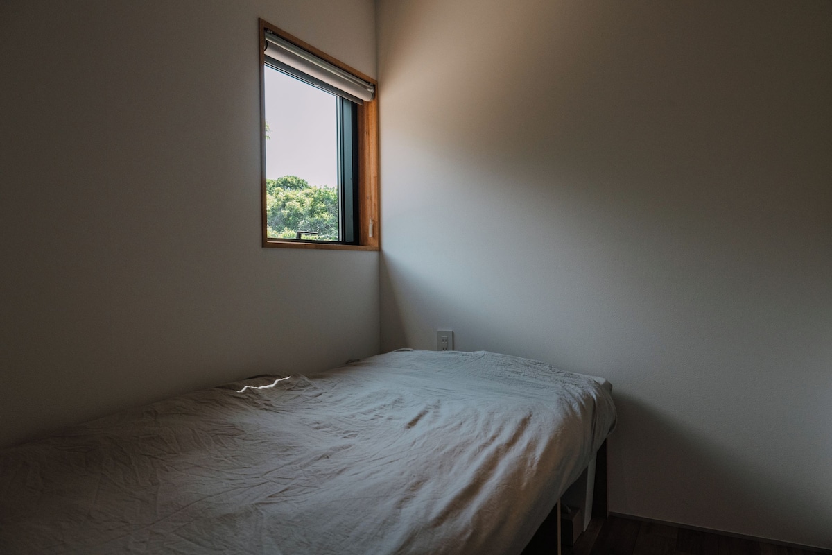 Una habitación pequeña y sencilla con una cama individual, una ventana y un enchufe en la pared.
