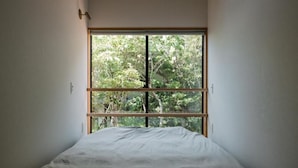 A bedroom with a large window, a bed, and a wall-mounted light fixture.