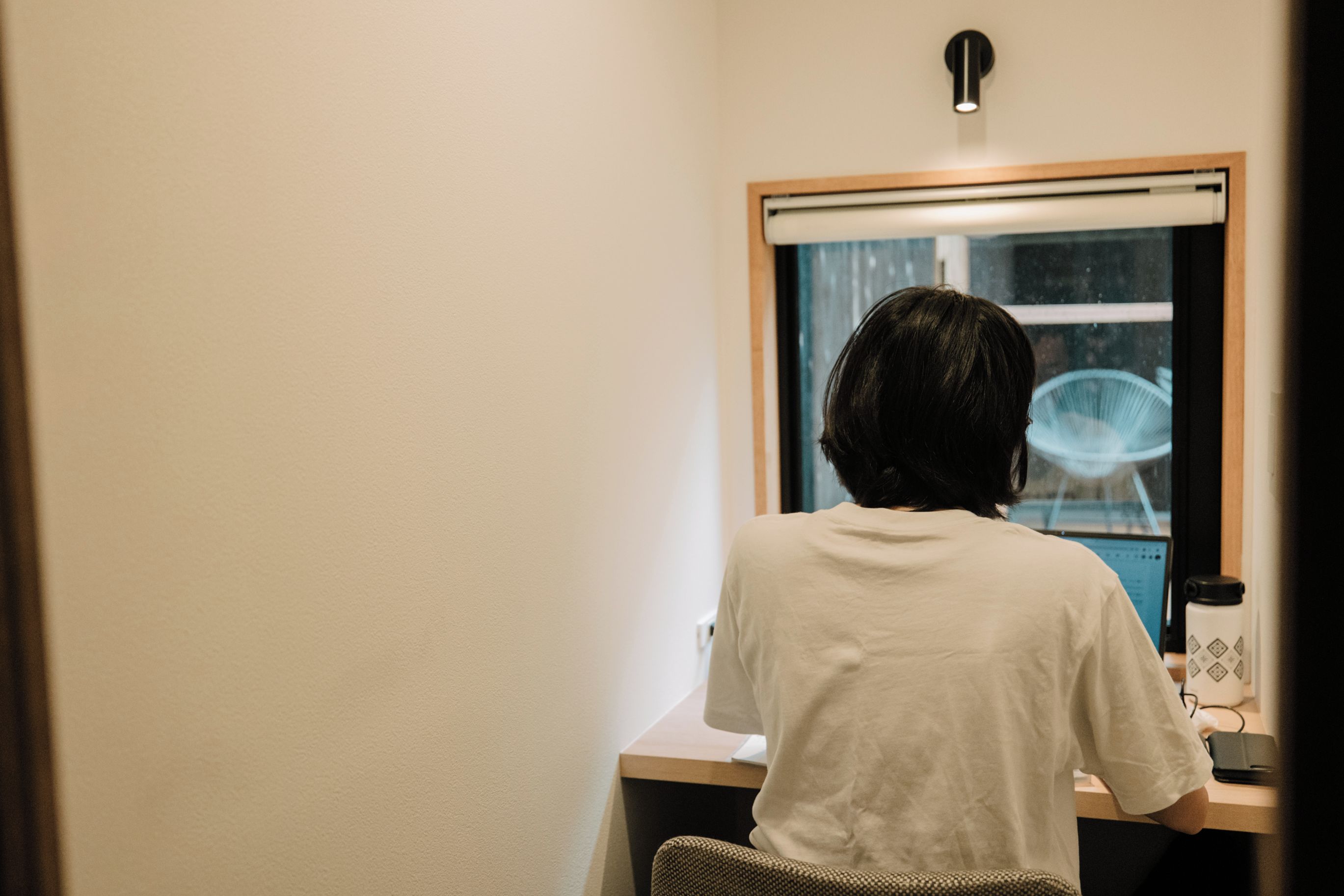 A person seated at a desk with a window, a lamp, and a water bottle.
