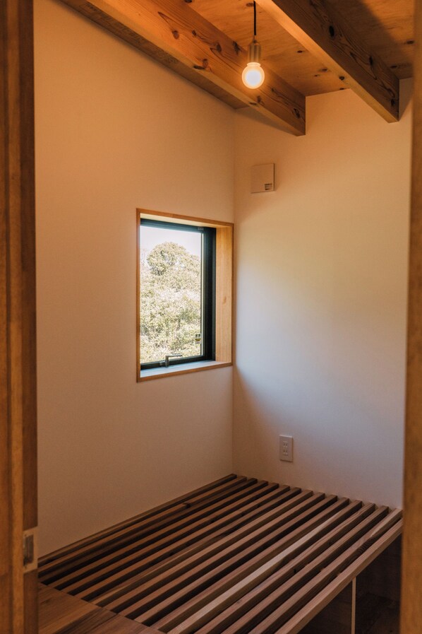 Una habitación con un banco de madera con listones, una ventana con vistas a árboles y una lámpara en el techo.